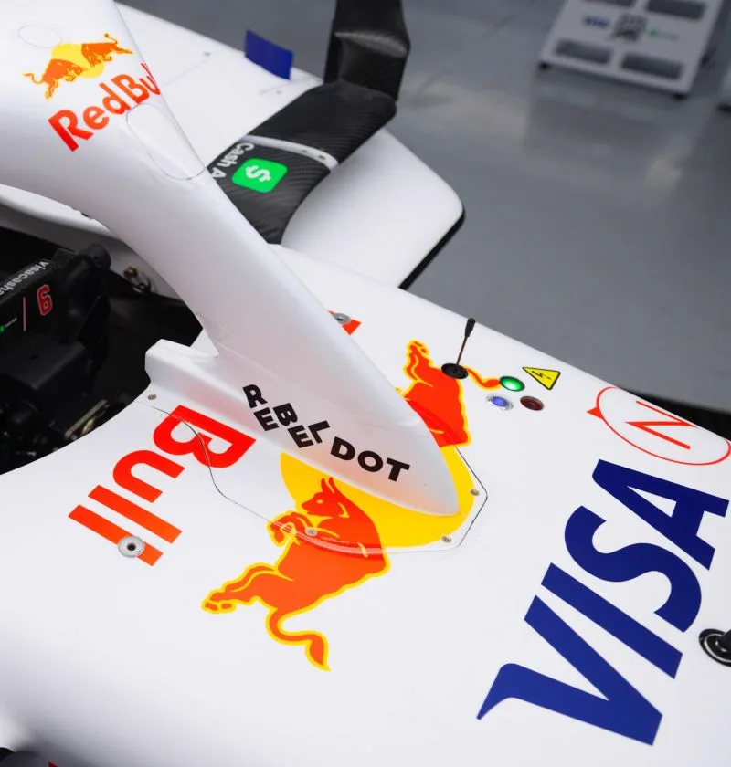 Close detail of the white engine cover and mirror stalk of a Visa Cash App Racing Bulls Formula One car in the garage, carrying the RebelDot, Red Bull and Visa markings.